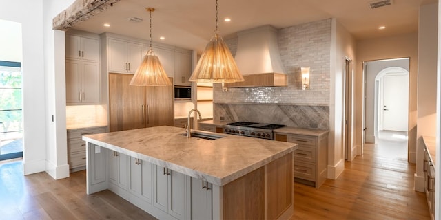 kitchen featuring custom range hood, a center island with sink, light countertops, and a sink