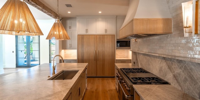 kitchen with custom range hood, high end stainless steel range oven, hanging light fixtures, white cabinets, and a sink