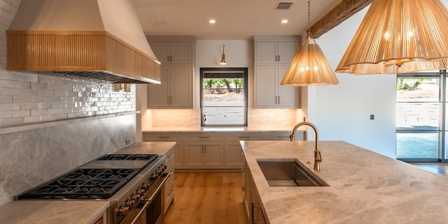 kitchen with light stone counters, range with two ovens, a sink, visible vents, and custom exhaust hood