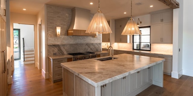 kitchen featuring light countertops, custom exhaust hood, an island with sink, and a sink