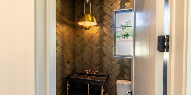 half bath featuring a sink, toilet, and wallpapered walls