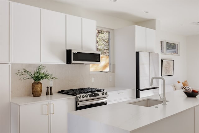 kitchen featuring light stone countertops, appliances with stainless steel finishes, backsplash, sink, and white cabinets