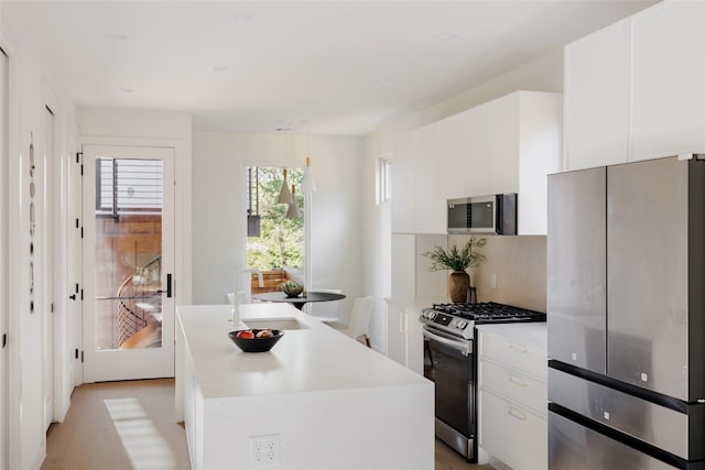 kitchen featuring a kitchen island with sink, white cabinets, sink, tasteful backsplash, and stainless steel appliances