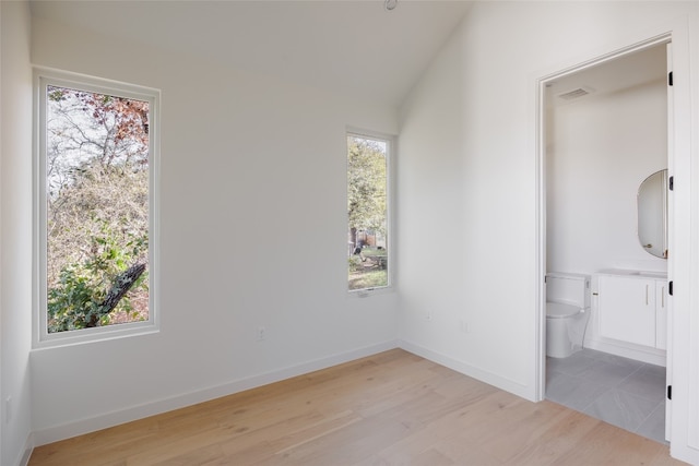 unfurnished bedroom with connected bathroom, light hardwood / wood-style flooring, and lofted ceiling