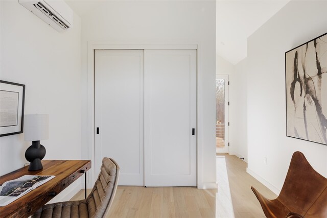 office area with light hardwood / wood-style floors, vaulted ceiling, and a wall mounted AC