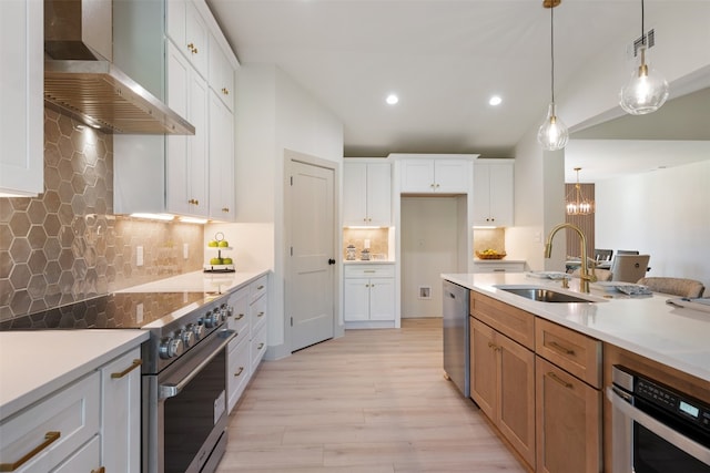 kitchen featuring stainless steel appliances, sink, wall chimney range hood, white cabinets, and hanging light fixtures