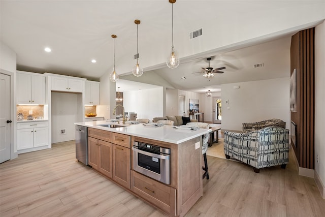 kitchen featuring sink, vaulted ceiling, a kitchen island with sink, white cabinets, and appliances with stainless steel finishes