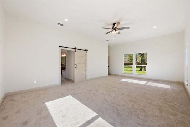 empty room with a barn door, light carpet, and ceiling fan