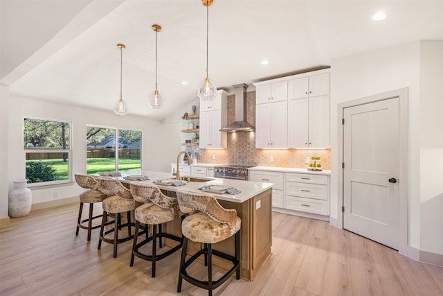 kitchen with light hardwood / wood-style flooring, white cabinets, wall chimney range hood, and a center island with sink