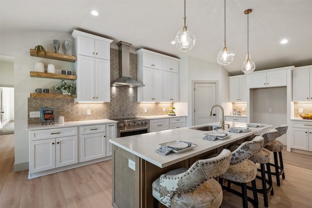 kitchen featuring vaulted ceiling, sink, wall chimney range hood, high end stainless steel range, and white cabinets