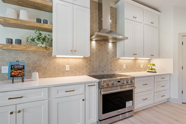 kitchen with tasteful backsplash, wall chimney range hood, electric range, light hardwood / wood-style floors, and white cabinetry