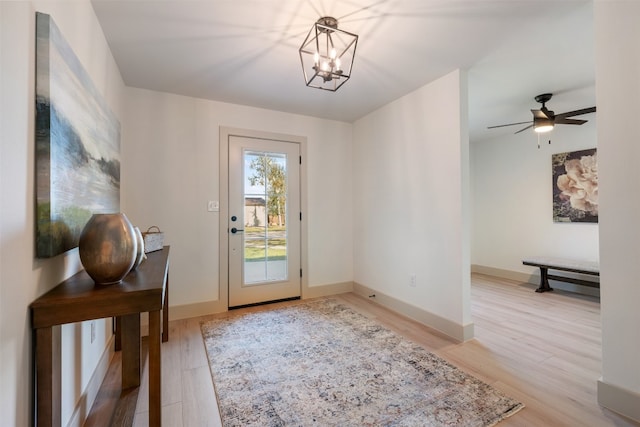 doorway to outside with ceiling fan with notable chandelier and light wood-type flooring