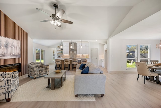 living room featuring ceiling fan with notable chandelier, light wood-type flooring, and lofted ceiling