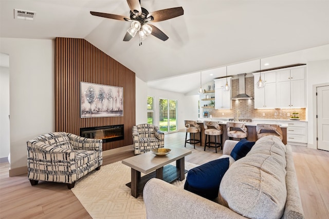 living room featuring ceiling fan, sink, vaulted ceiling, and light wood-type flooring