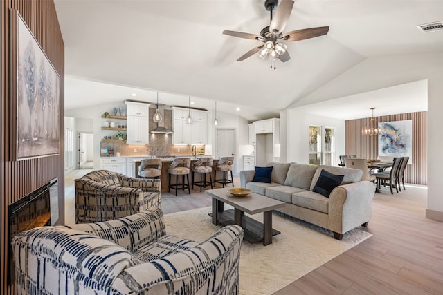 living room with ceiling fan with notable chandelier, light wood-type flooring, vaulted ceiling, and sink