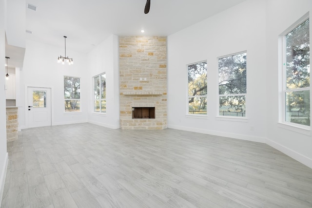 unfurnished living room with a fireplace, a healthy amount of sunlight, ceiling fan with notable chandelier, and light wood-type flooring