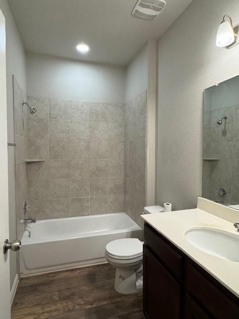 full bathroom featuring hardwood / wood-style floors, vanity, toilet, and tiled shower / bath