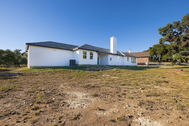 rear view of house with central AC unit and a lawn