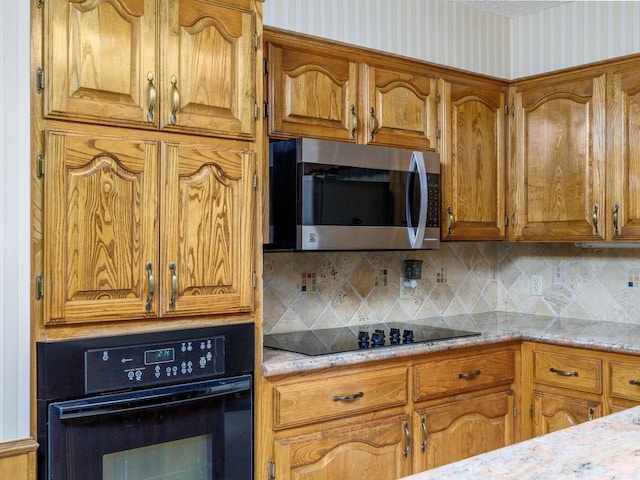 kitchen featuring black appliances, decorative backsplash, and light stone counters