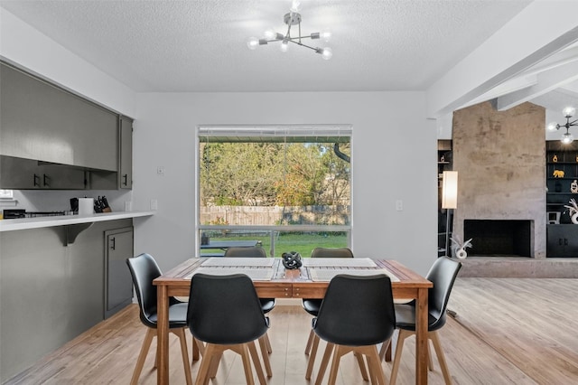 dining area with light hardwood / wood-style flooring, a fireplace, a textured ceiling, beamed ceiling, and a notable chandelier