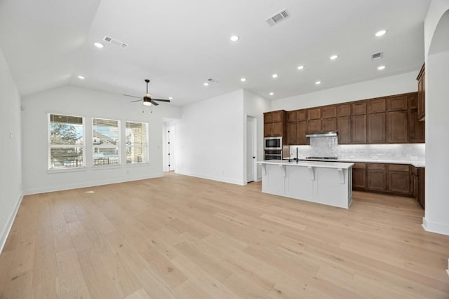 kitchen with a breakfast bar, appliances with stainless steel finishes, a kitchen island with sink, light hardwood / wood-style floors, and decorative backsplash