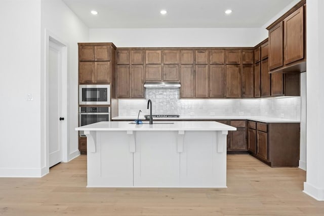 kitchen featuring a kitchen island with sink, built in microwave, oven, and decorative backsplash