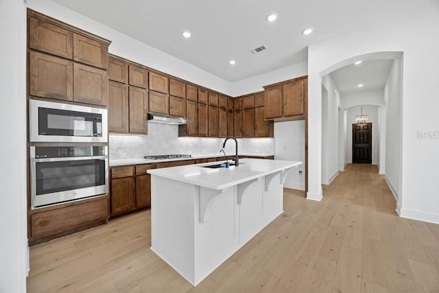 kitchen with appliances with stainless steel finishes, tasteful backsplash, sink, a breakfast bar area, and a center island with sink