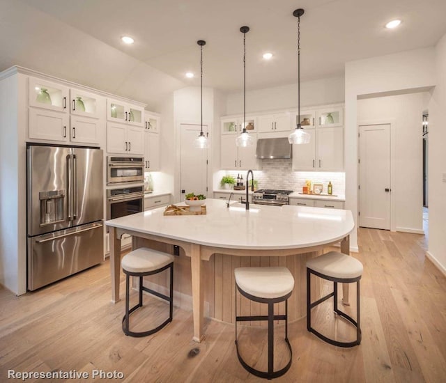 kitchen with high quality appliances, white cabinets, an island with sink, and wall chimney range hood