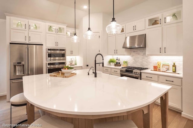 kitchen with a center island with sink, wall chimney exhaust hood, white cabinetry, and appliances with stainless steel finishes