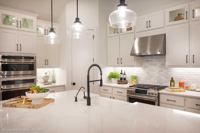 kitchen with sink, wall chimney exhaust hood, appliances with stainless steel finishes, decorative light fixtures, and white cabinetry