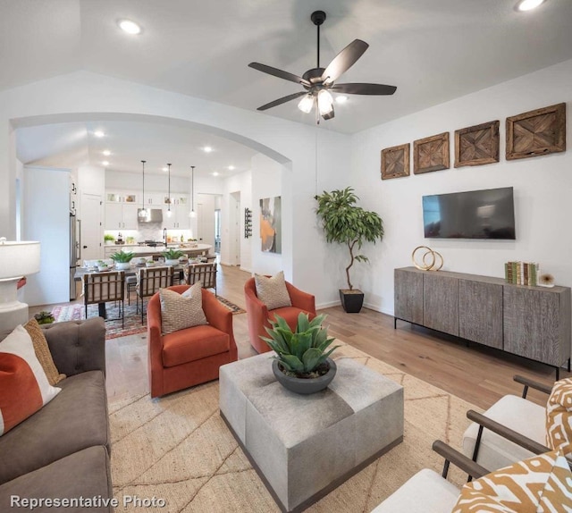 living room with ceiling fan, light hardwood / wood-style flooring, and vaulted ceiling