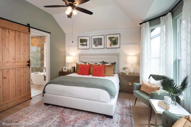 bedroom featuring ensuite bath, ceiling fan, a barn door, hardwood / wood-style floors, and lofted ceiling