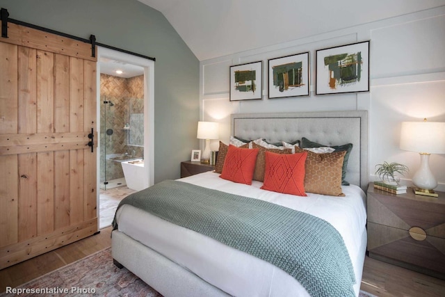 bedroom with hardwood / wood-style flooring, a barn door, lofted ceiling, and connected bathroom