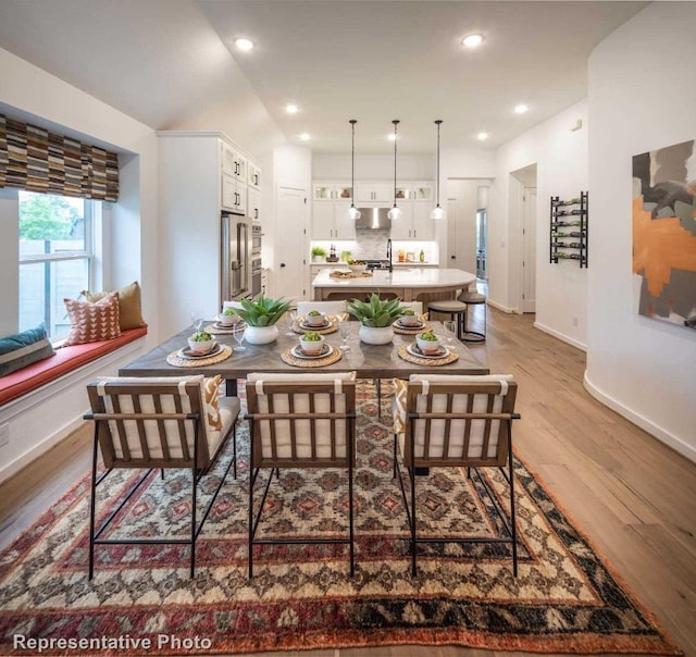 dining space with sink, light hardwood / wood-style floors, and vaulted ceiling