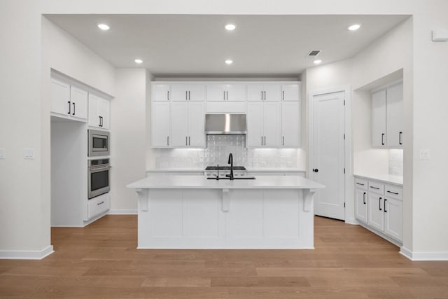 kitchen with light countertops, under cabinet range hood, a sink, backsplash, and stainless steel appliances