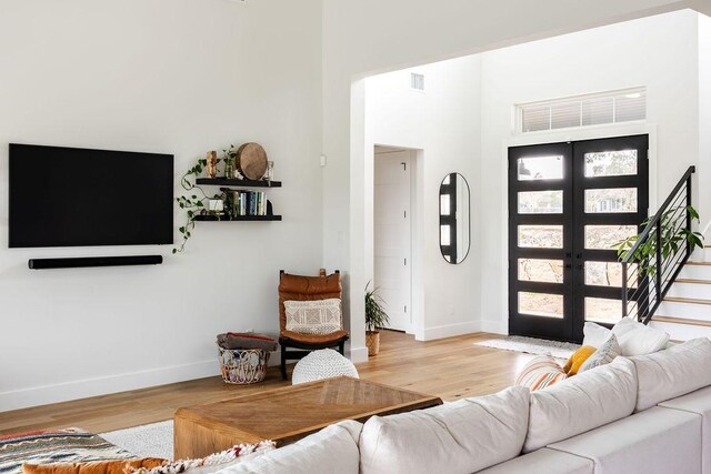 living room with a high ceiling, light hardwood / wood-style floors, and french doors