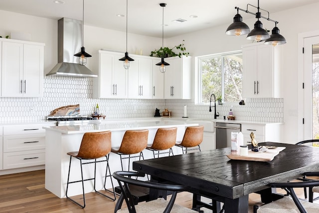 kitchen with a center island, white cabinets, wall chimney exhaust hood, appliances with stainless steel finishes, and wood-type flooring