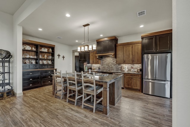 kitchen featuring hardwood / wood-style floors, a center island with sink, hanging light fixtures, a kitchen bar, and stainless steel appliances