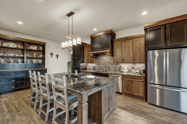 kitchen featuring a kitchen bar, stainless steel appliances, a kitchen island with sink, pendant lighting, and dark stone countertops