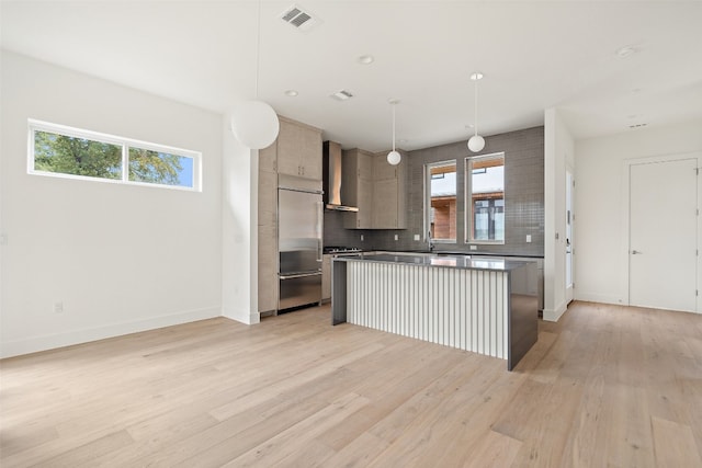 kitchen with wall chimney range hood, built in fridge, pendant lighting, light hardwood / wood-style floors, and a kitchen island