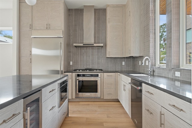 kitchen with wall chimney range hood, sink, light hardwood / wood-style flooring, appliances with stainless steel finishes, and beverage cooler