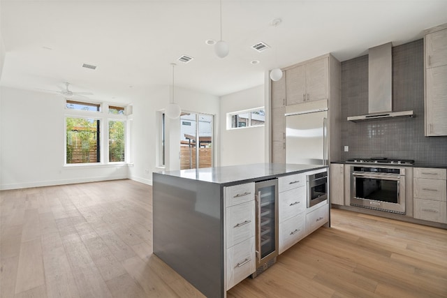 kitchen featuring appliances with stainless steel finishes, wall chimney range hood, light hardwood / wood-style floors, wine cooler, and hanging light fixtures