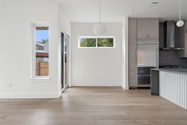 kitchen with built in fridge, plenty of natural light, pendant lighting, and wall chimney range hood