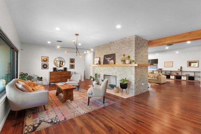 living room featuring a chandelier, hardwood / wood-style flooring, a stone fireplace, and beamed ceiling