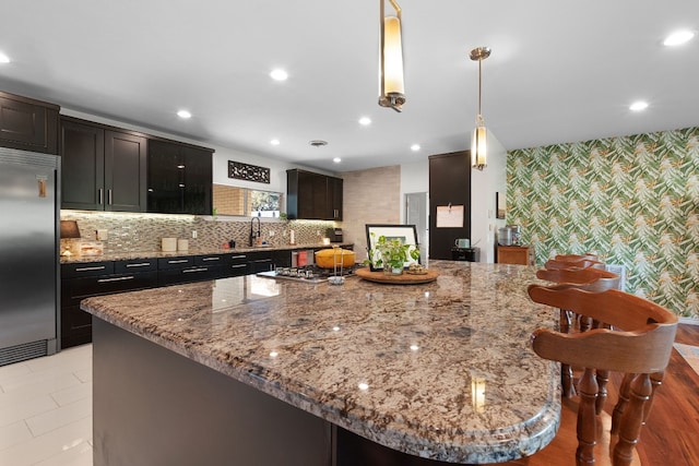 kitchen featuring light stone countertops, sink, stainless steel appliances, pendant lighting, and light hardwood / wood-style floors