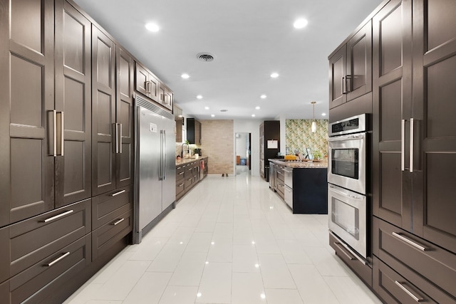 kitchen featuring sink, backsplash, pendant lighting, dark brown cabinets, and appliances with stainless steel finishes