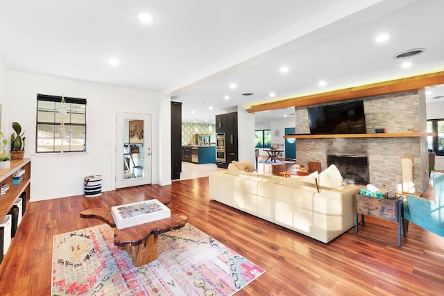 living room featuring light hardwood / wood-style floors, a stone fireplace, and a healthy amount of sunlight