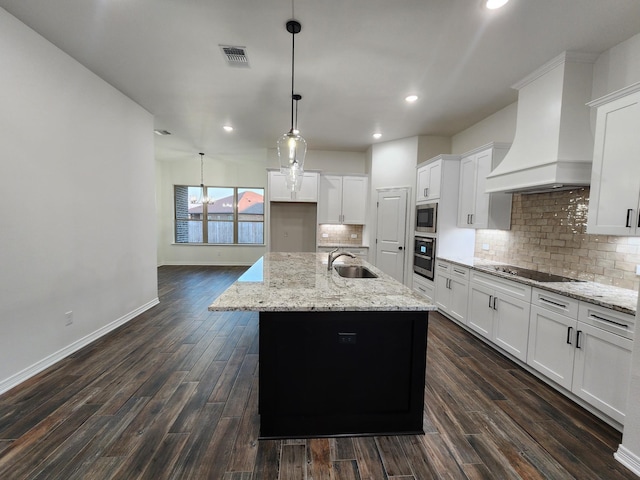 kitchen featuring white cabinetry, custom range hood, decorative light fixtures, an island with sink, and stainless steel appliances