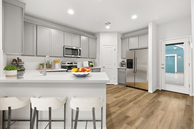 kitchen with appliances with stainless steel finishes, a kitchen bar, kitchen peninsula, and gray cabinets