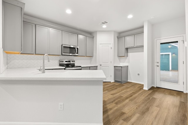 kitchen featuring appliances with stainless steel finishes, gray cabinetry, backsplash, kitchen peninsula, and light hardwood / wood-style flooring